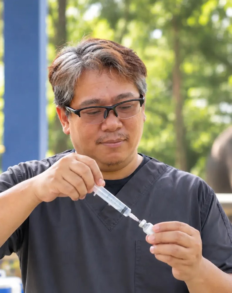 Person in dark scrubs outdoors drawing liquid into syringe.